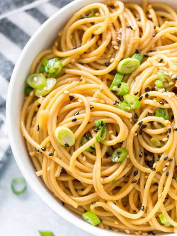 close up of sesame noodles in a white bowl topped with green onion and black sesame seeds