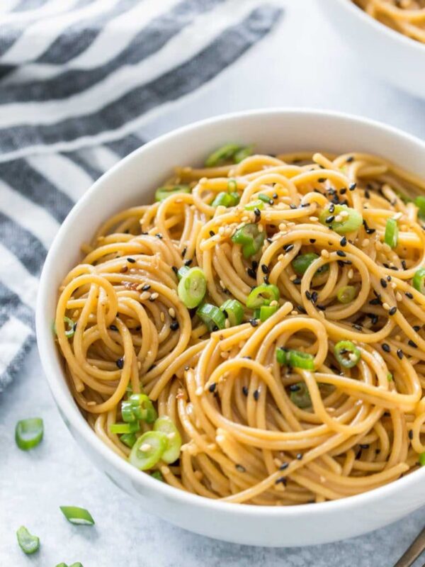 sesame noodles in a white bowl topped with green onion and black sesame seeds