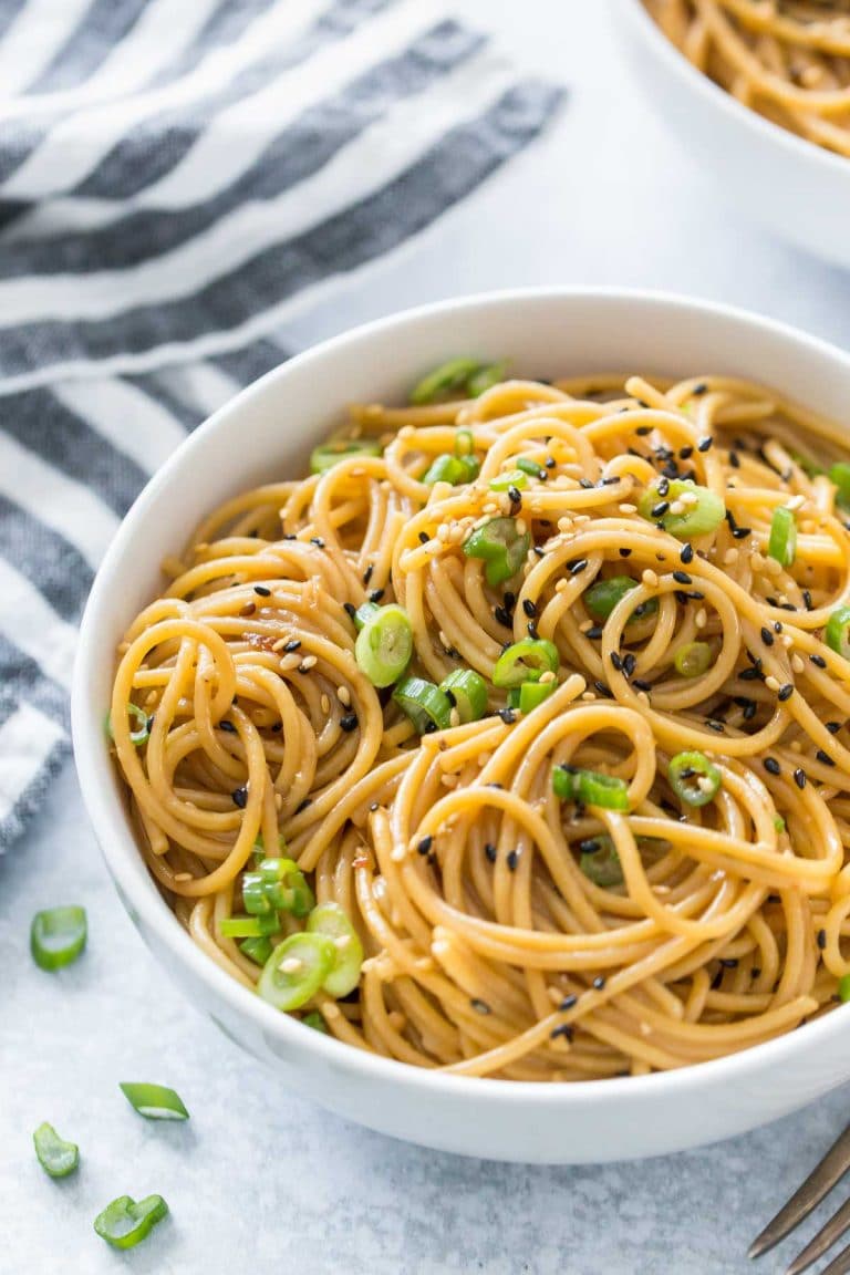 sesame noodles in a white bowl topped with green onion and black sesame seeds