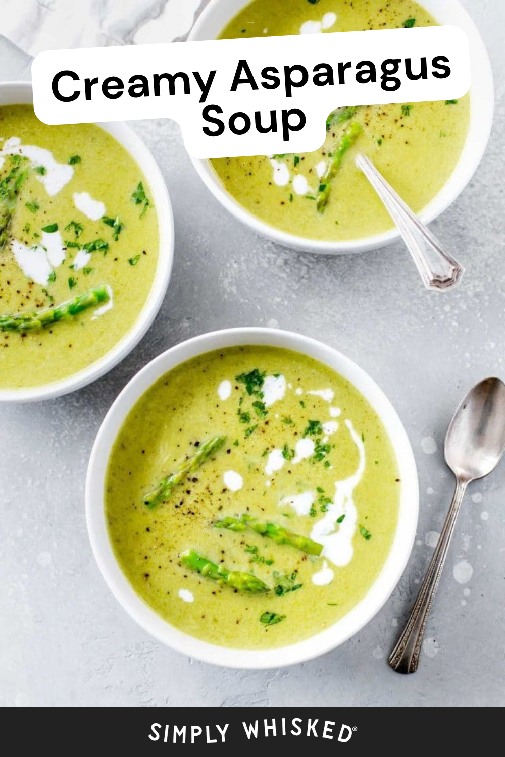 Three bowls of creamy asparagus soup, garnished with tender asparagus tips, fresh herbs, and delicate drizzles of cream, sit on a gray surface with spoons nearby. The text reads “Creamy Asparagus Soup” and “Simply Whisked.”.