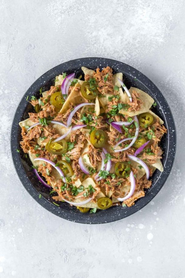 bbq pulled pork nachos waiting for dairy free cheese to go in the oven in a black speckled pie plate
