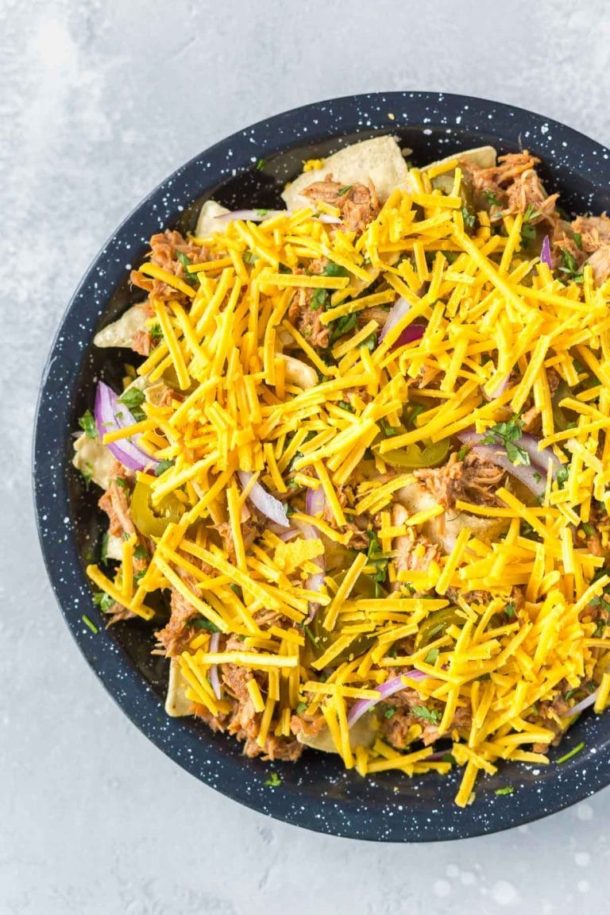bbq pulled pork nachos ready to go in the oven in a black speckled pie plate