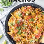 BBQ pulled pork nachos in a black speckled pie plate on a white and blue dish towel with lime wedges to the side and a small bowl of cilantro, optimized for Pinterest with text overlay