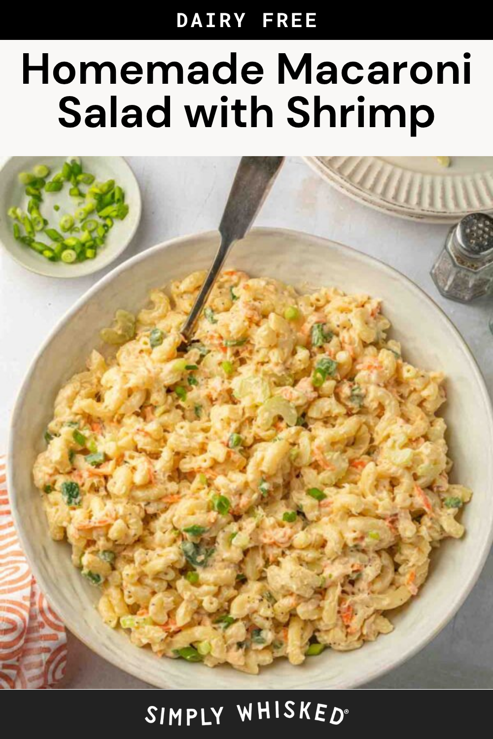 A large bowl of this easy macaroni salad with shrimp is topped with chopped green onions, making it a delicious and refreshing dish. A fork rests in the bowl, and a small dish of extra green onions sits nearby. The macaroni salad recipe is beautifully presented on a light table with an orange-striped cloth.