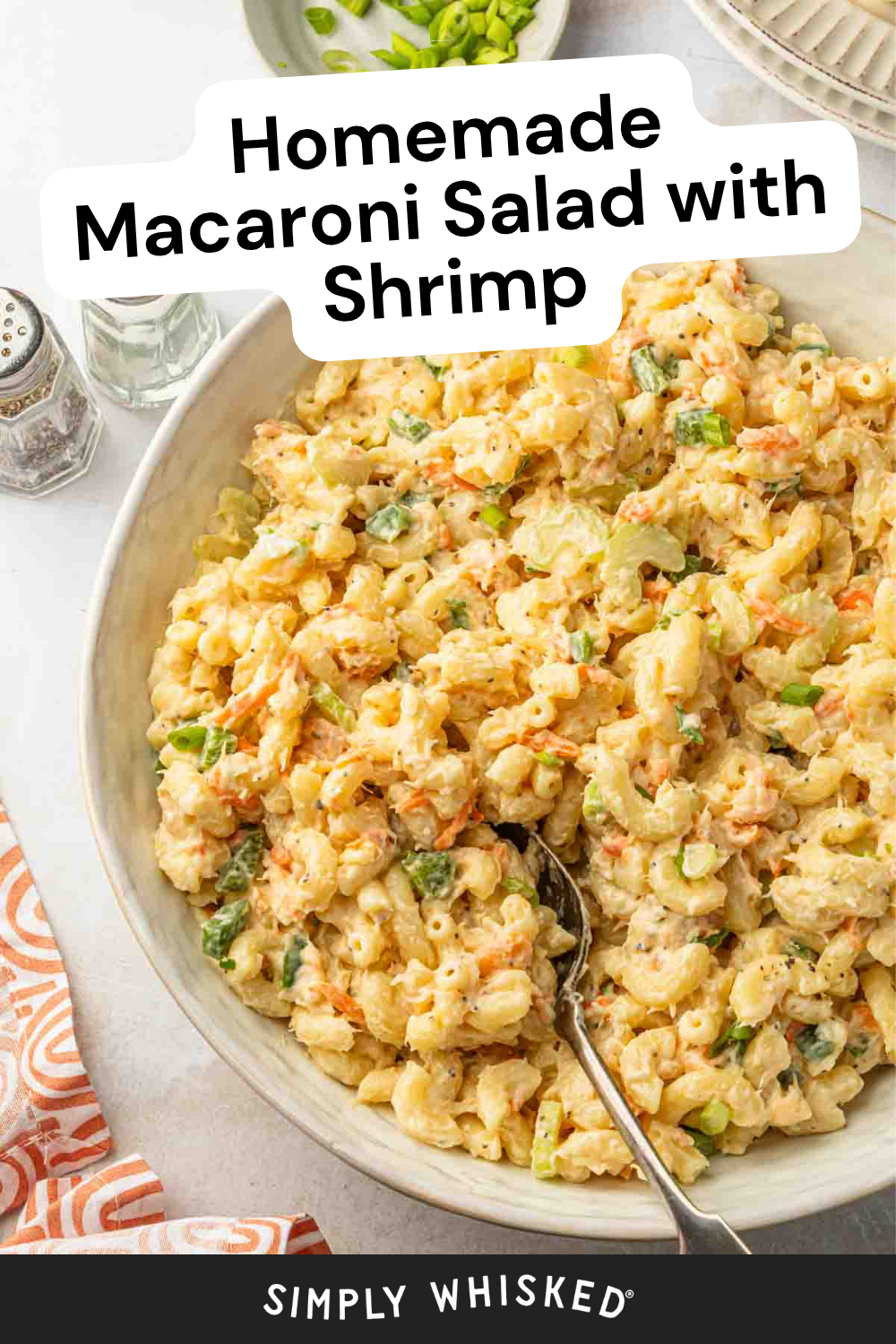 A large bowl of macaroni salad with shrimp, chopped vegetables, and a creamy dressing sits ready to serve—the perfect easy macaroni salad recipe. A spoon rests in the bowl with a napkin, salt, and pepper nearby.