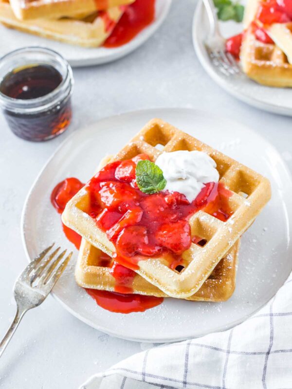 two homemade waffles topped with strawberry sauce and dairy free whipped cream