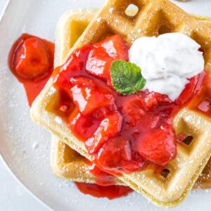two homemade waffles topped with strawberry sauce and dairy free whipped cream
