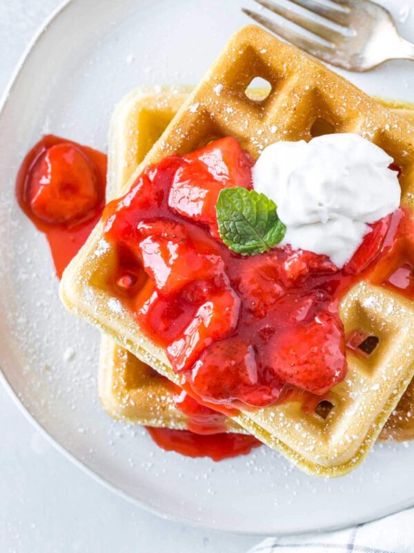 two homemade waffles topped with strawberry sauce and dairy free whipped cream