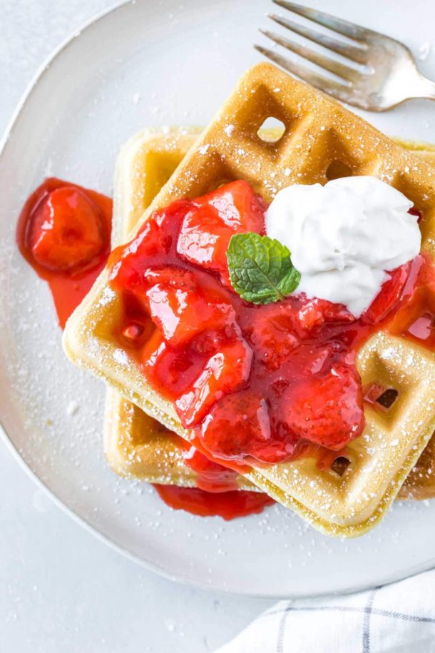 two homemade waffles topped with strawberry sauce and dairy free whipped cream