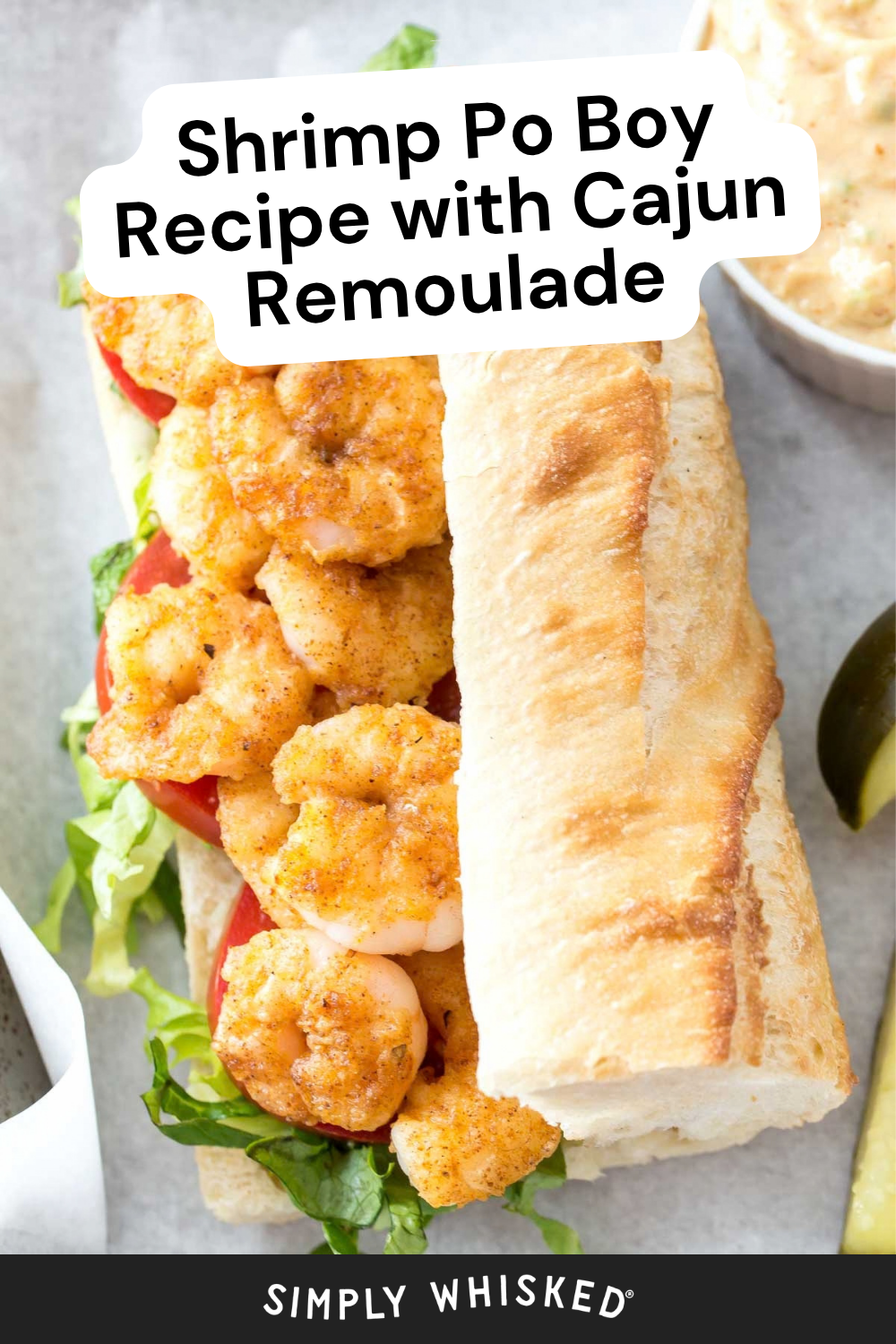 A classic shrimp po boy recipe featuring a baguette filled with crispy fried shrimp, fresh lettuce, and ripe tomato, served alongside zesty Cajun remoulade sauce and a crisp pickle spear. Text reads: Shrimp Po Boy Recipe with Cajun Remoulade.