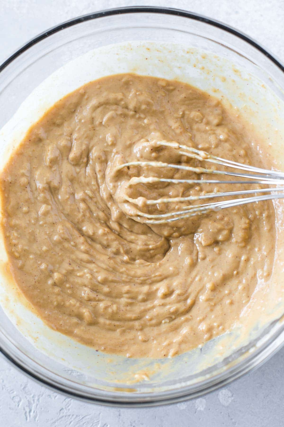 thai peanut sauce being whisked in a clear bowl on a gray painted surface