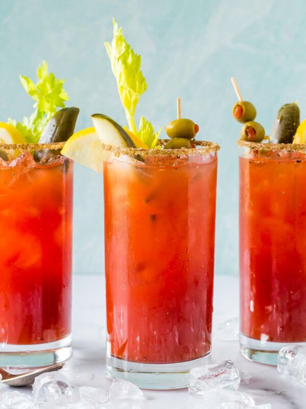 3 garnished bloody caesar drinks on a marble surface with light blue background