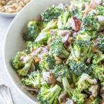 close up of broccoli salad with bacon and grapes in a large white serving bowl, with text overlay for Pinterest that reads "easy broccoli salad, dairy free, whole 30 and paleo friendly"
