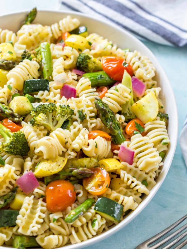 close up of a vegan, roasted vegetable pasta salad in a white bowl on a blue surface
