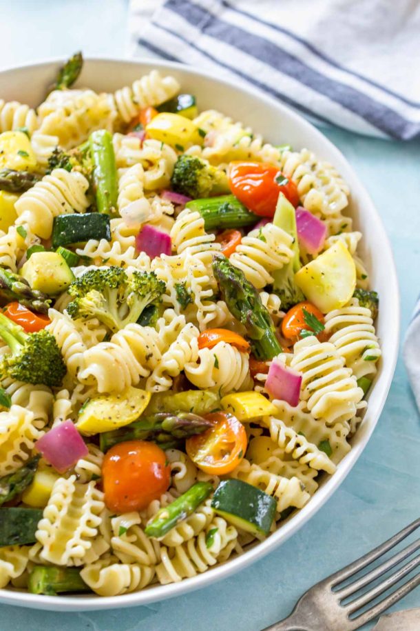 close up of a vegan, roasted vegetable pasta salad in a white bowl on a blue surface