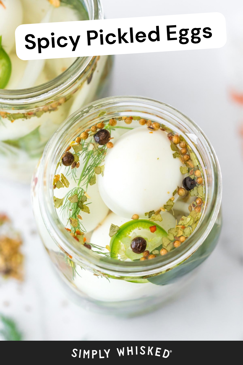 Two glass jars filled with hard-boiled eggs, dill, peppercorns, coriander seeds, and sliced jalapeños in clear brine are labeled spicy pickled eggs.