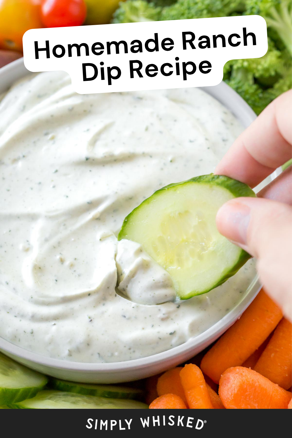 A hand dips a cucumber slice into a bowl of creamy ranch dip made with homemade ranch seasoning, surrounded by fresh vegetables like carrots and broccoli. Text reads Homemade Ranch Dip Recipe and Simply Whisked.