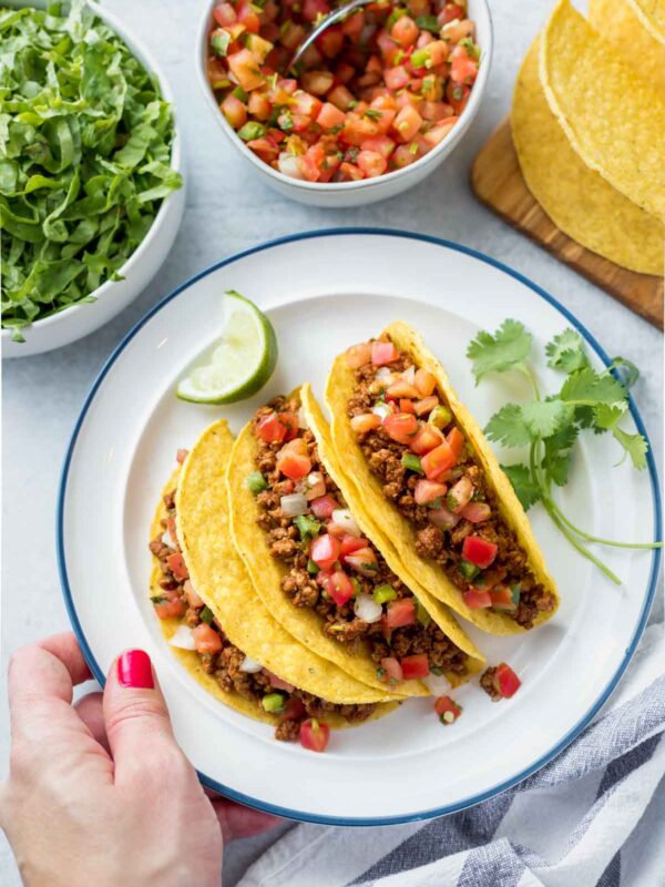 tacos made with ground chicken served on a white plate in crispy, corn tortillas with pico de gallo