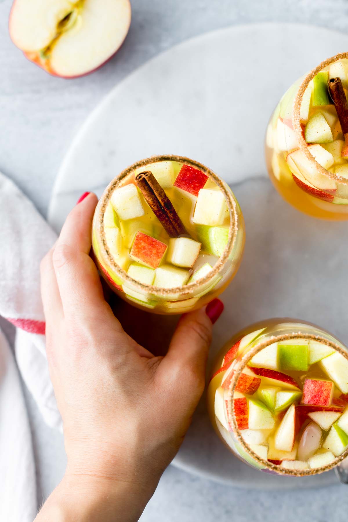 hand taking a apple cider sangria garnished with a cinnamon stick from a marble tray