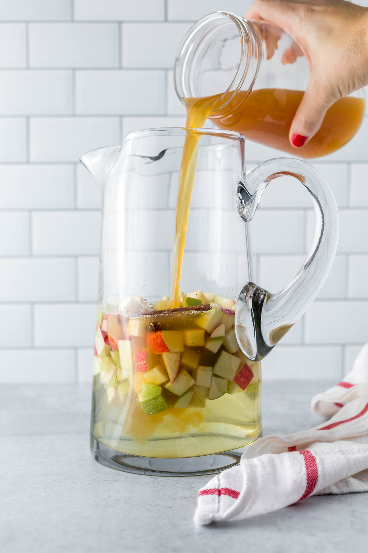 adding apple cider to a pitcher to make fall sangria