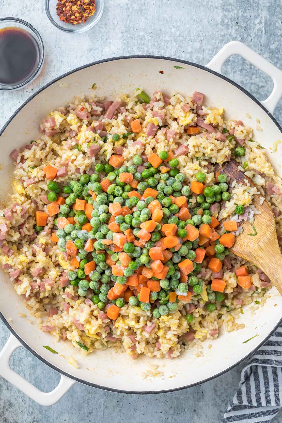 adding frozen peas and carrots to a ham fried rice recipe in a large white skillet