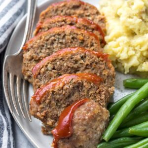 closeup of mini meatloaf recipe, sliced on a plate with green beans and mashed potatoes
