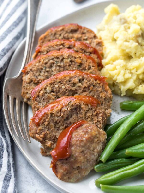 closeup of mini meatloaf recipe, sliced on a plate with green beans and mashed potatoes