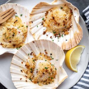 baked scallops in the shell on a gray plate with a lemon wedge