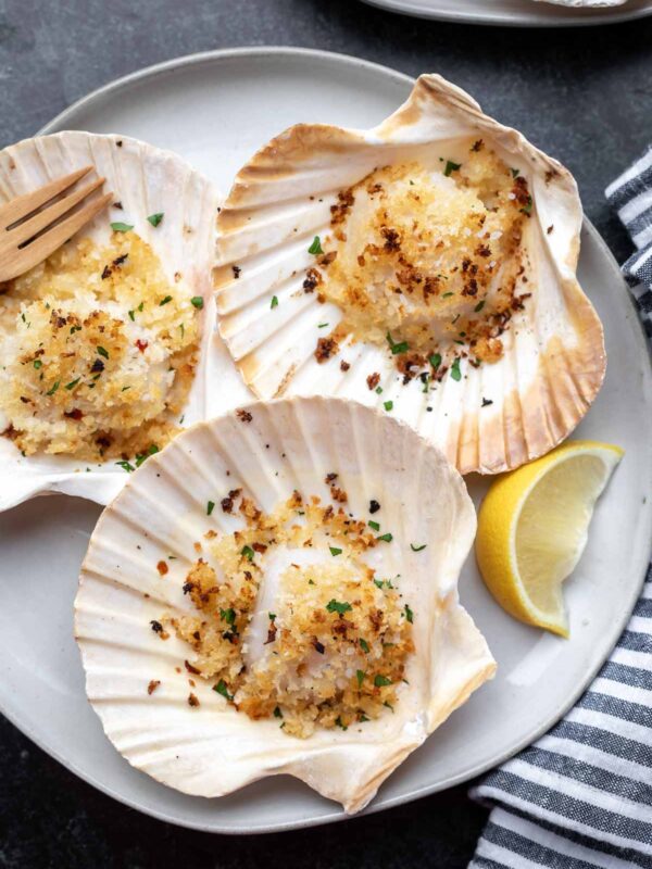 baked scallops in the shell on a gray plate with a lemon wedge