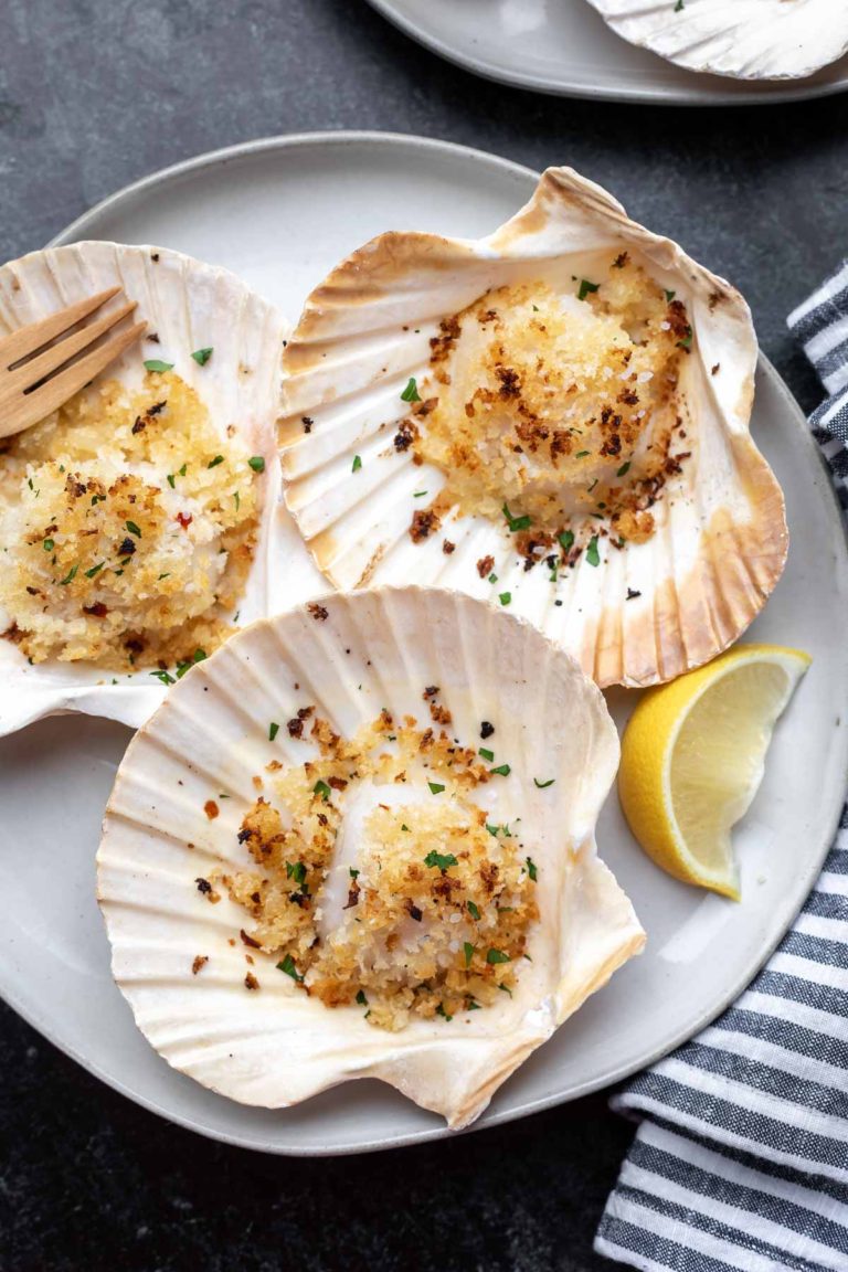 baked scallops in the shell on a gray plate with a lemon wedge