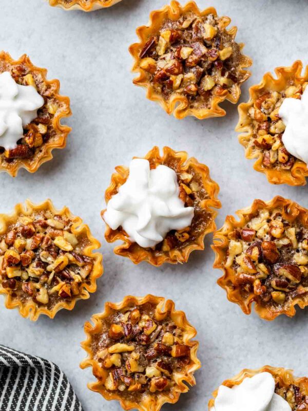 pecan pie bites on a gray surface, some topped with dairy free whipped cream