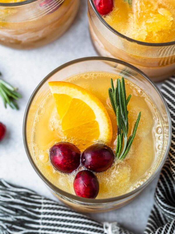 a top view of a cup full of brandy slush with garnishes of sliced orange rosemary and cranberries