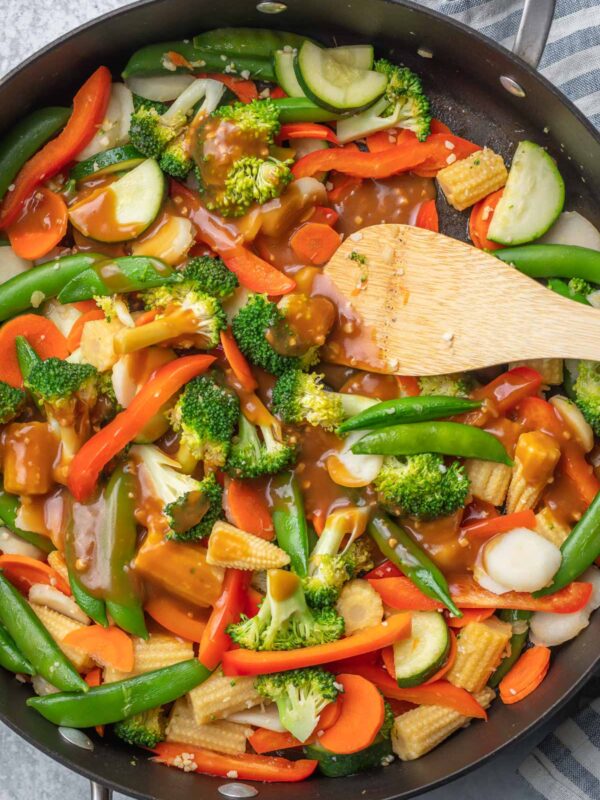 a sillet with mixed vegetables covered in soy sauce and a wooden spoon
