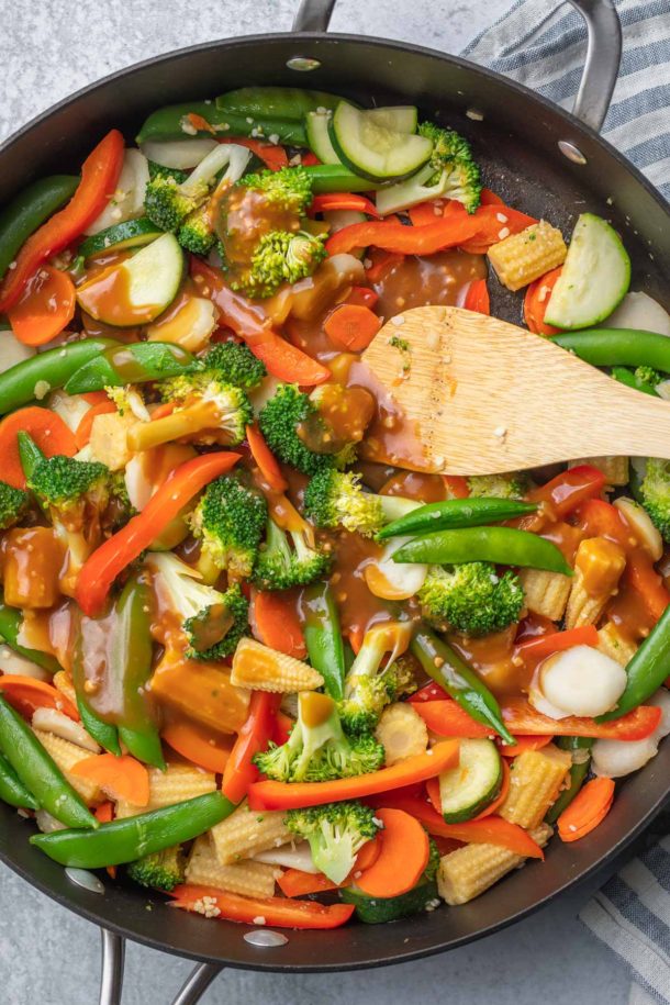 a sillet with mixed vegetables covered in soy sauce and a wooden spoon