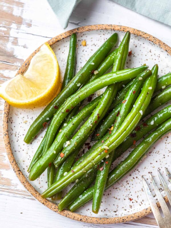 a plate of cooked italian green beans with a side of lemon slice