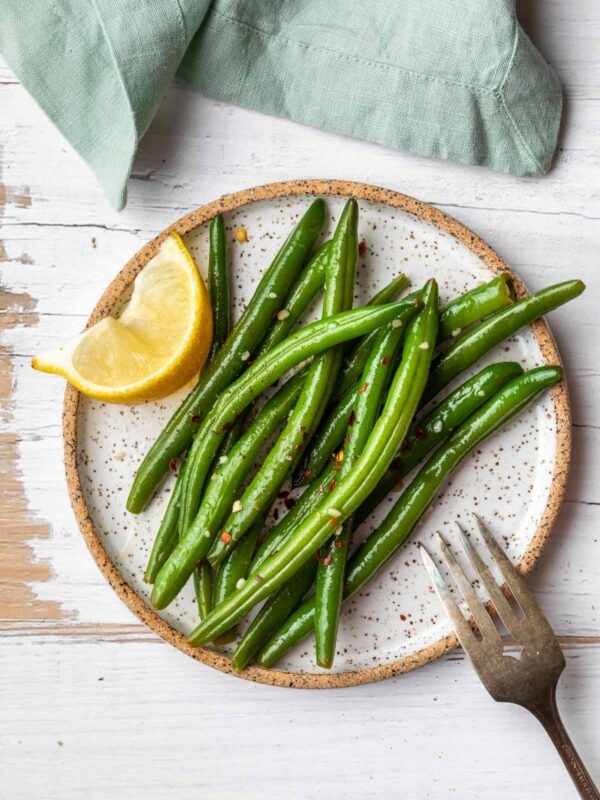 an aerial view of a plate of italian green beans with a slice of lemon and a fork