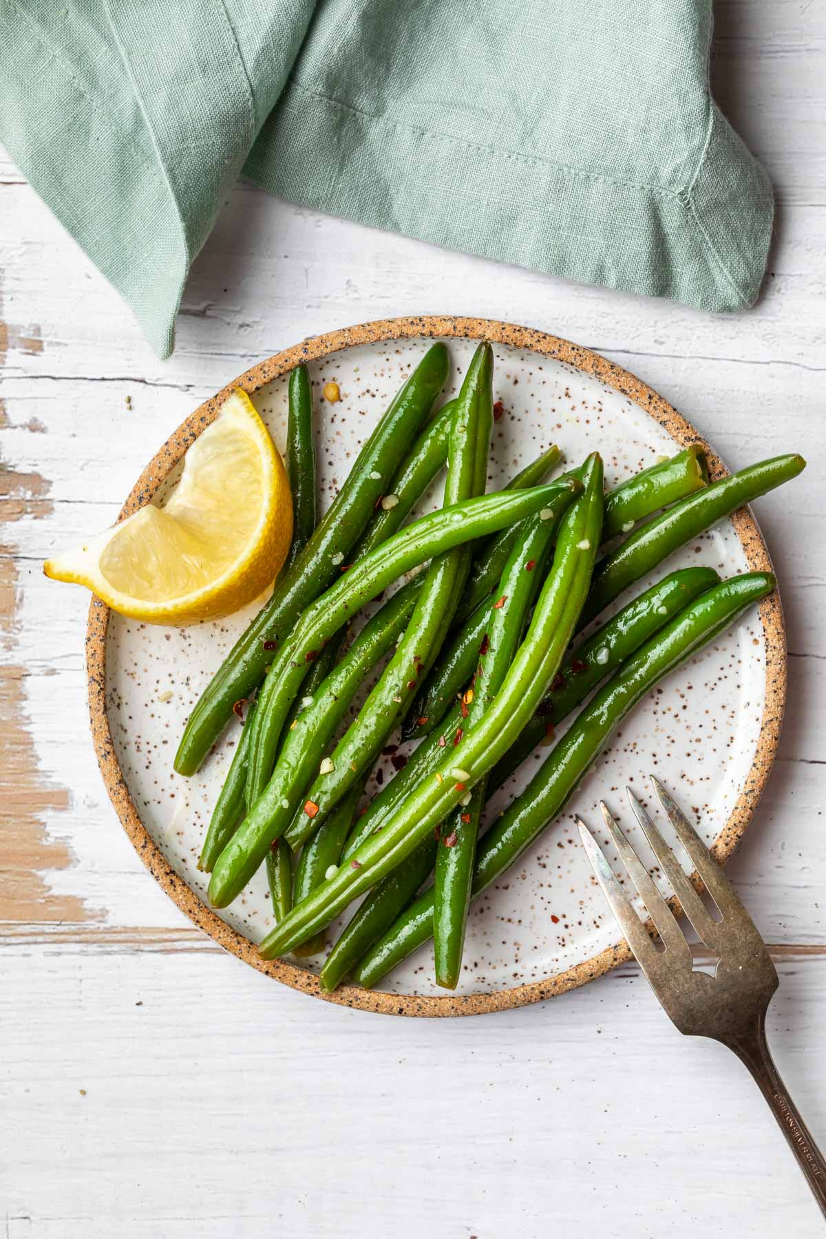 an aerial view of a plate of italian green beans with a slice of lemon and a fork