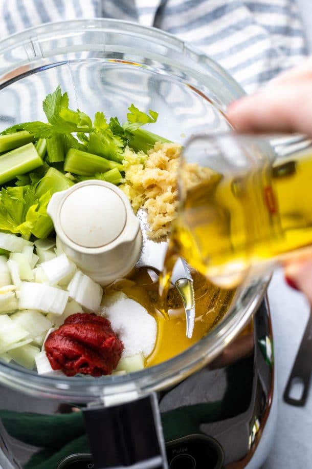 pouring olive oil into a food processor full of dressing ingredients