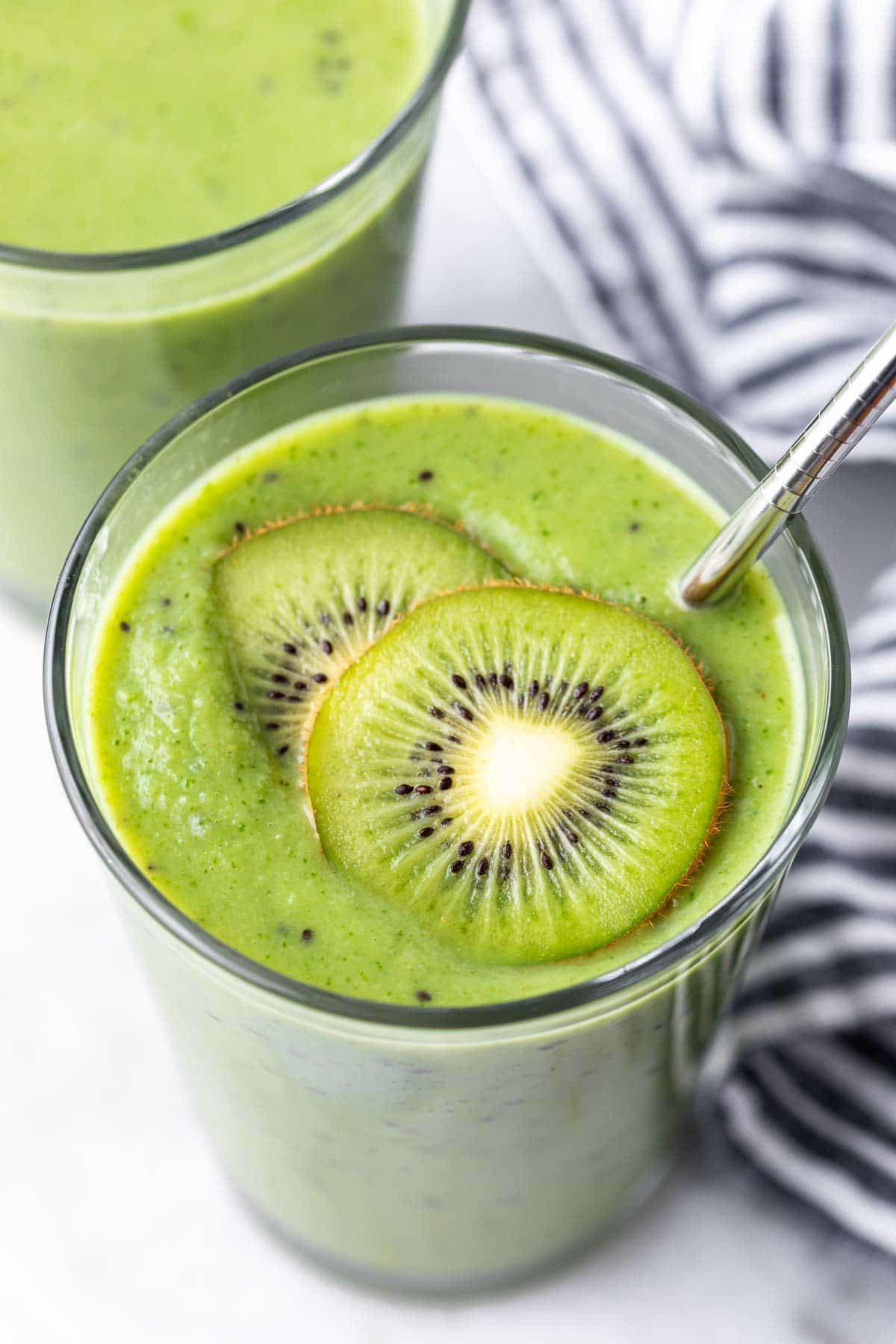 a glass full of kiwi smoothie and topped with two kiwi slices