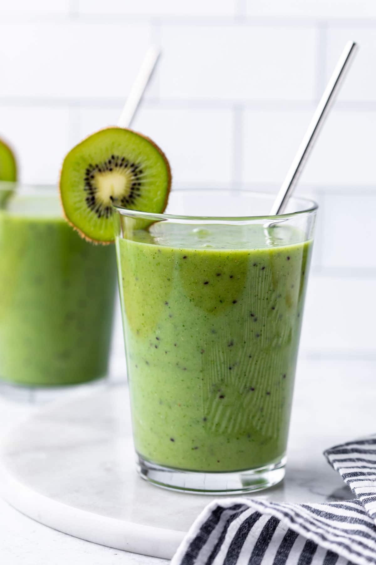 a glass full of kiwi smoothie with a sliced kiwi on the rim