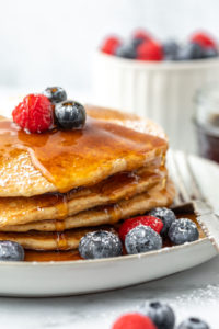 a close view of a stack of pancakes covered in syrup and garnished with berries