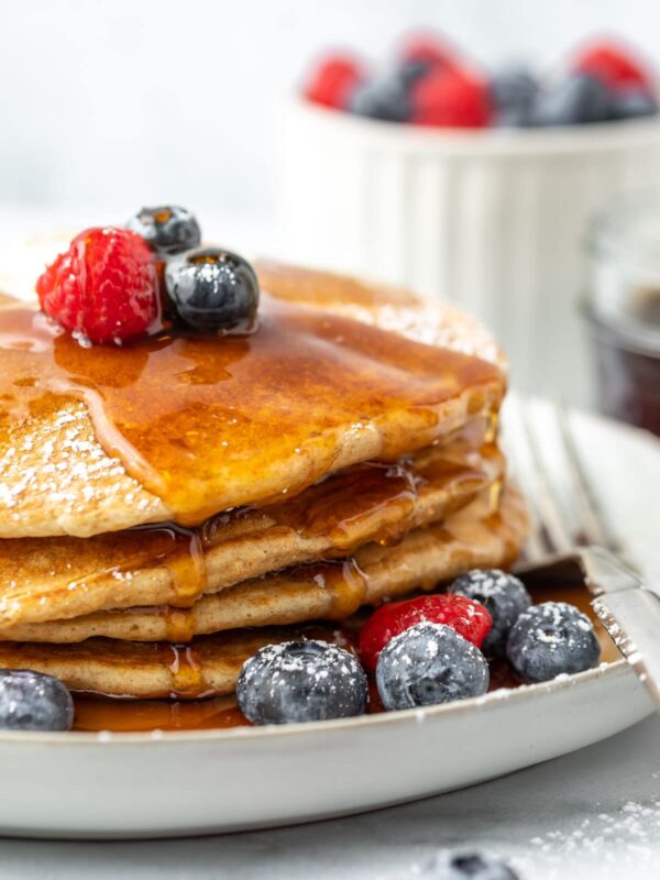 a close view of a stack of pancakes covered in syrup and garnished with berries