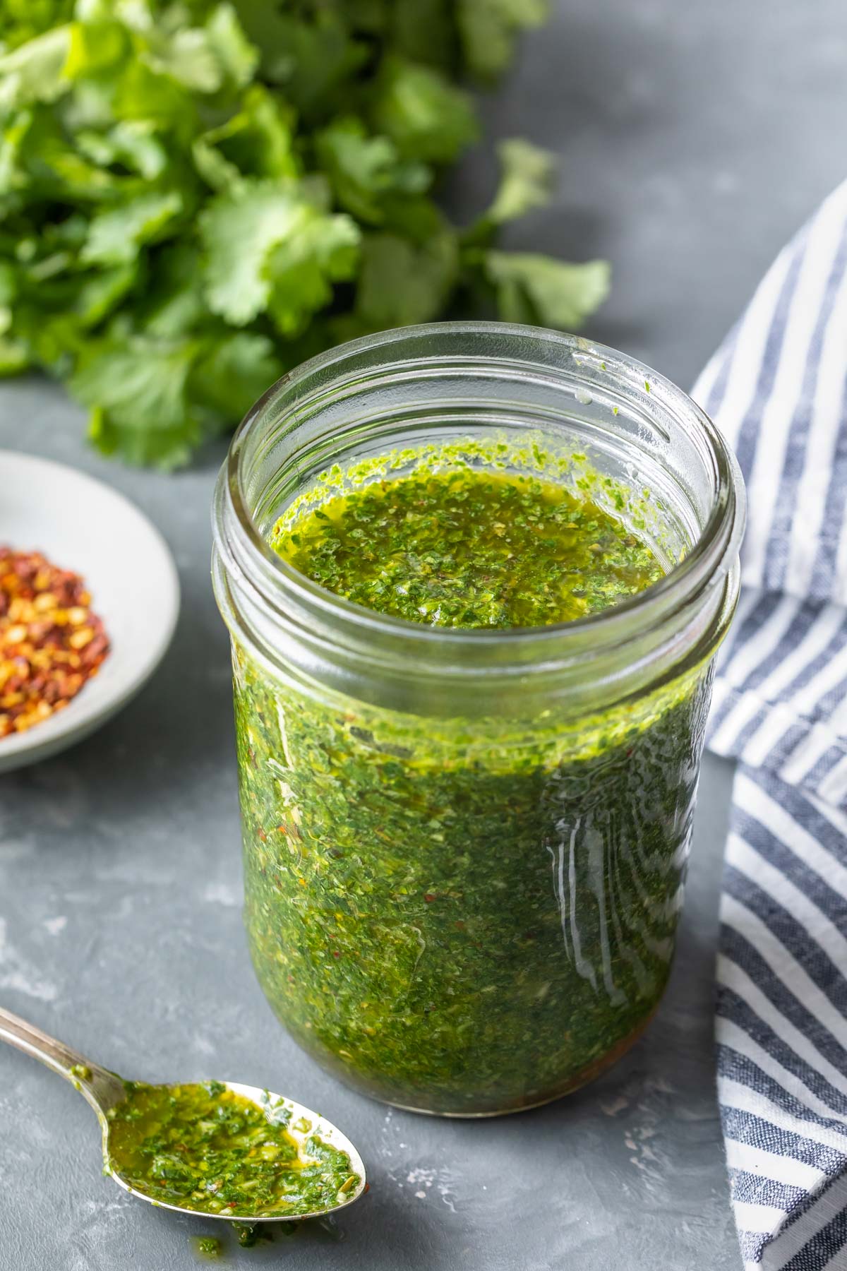 chimichurri sauce in a jar with a covered spoon to the side