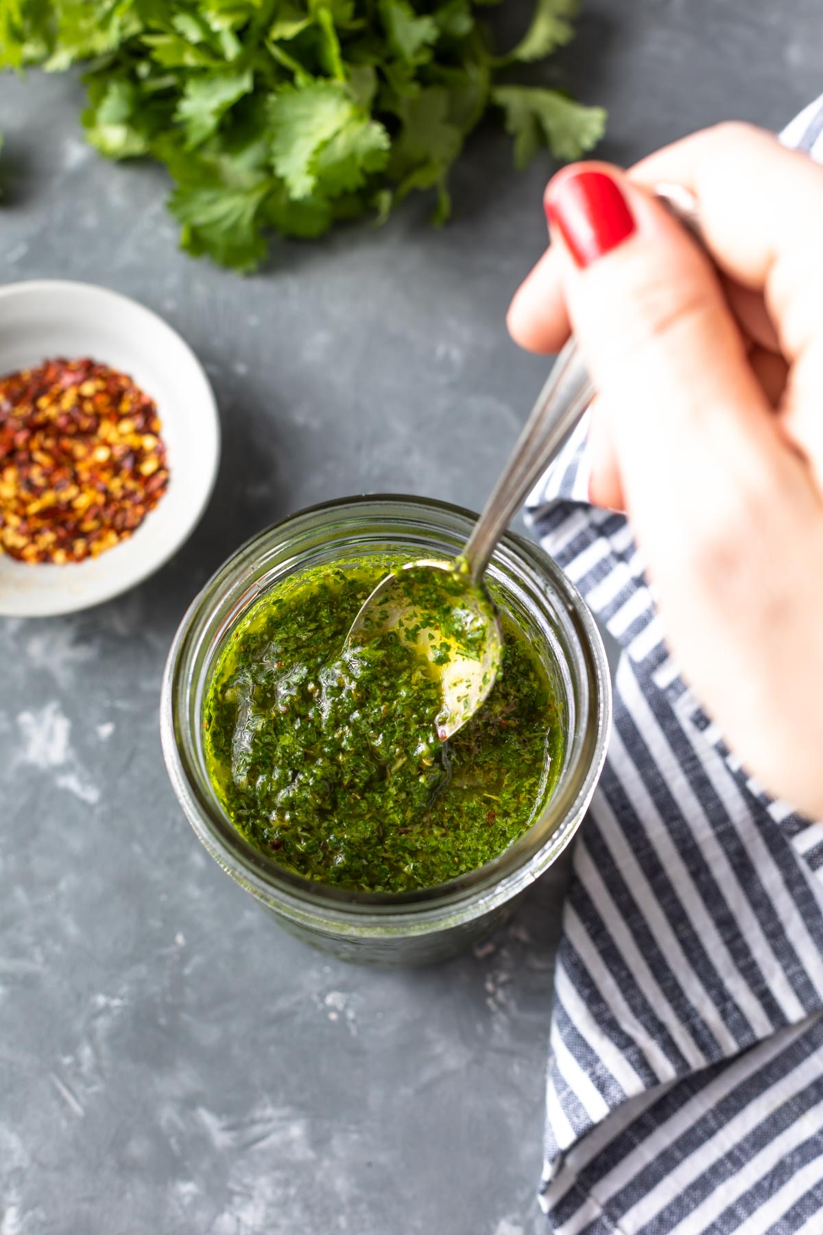 dipping a spoon into a jar of chimichurri sauce