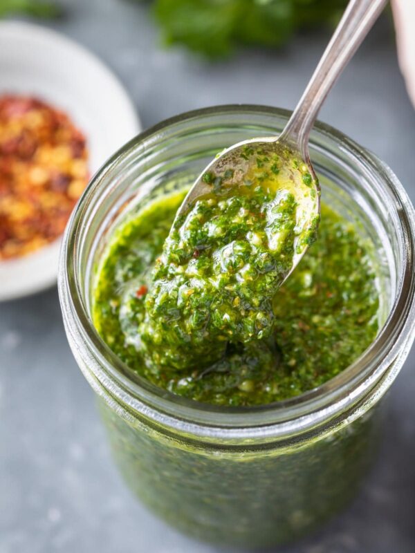 pouring chimichurri sauce off a spoon into a filled jar