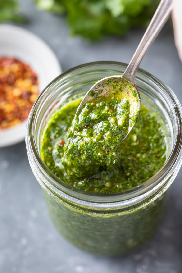 pouring chimichurri sauce off a spoon into a filled jar