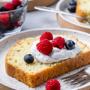 a close up side view of plates with french yogurt cake slices topped with whipped cream and fresh berries