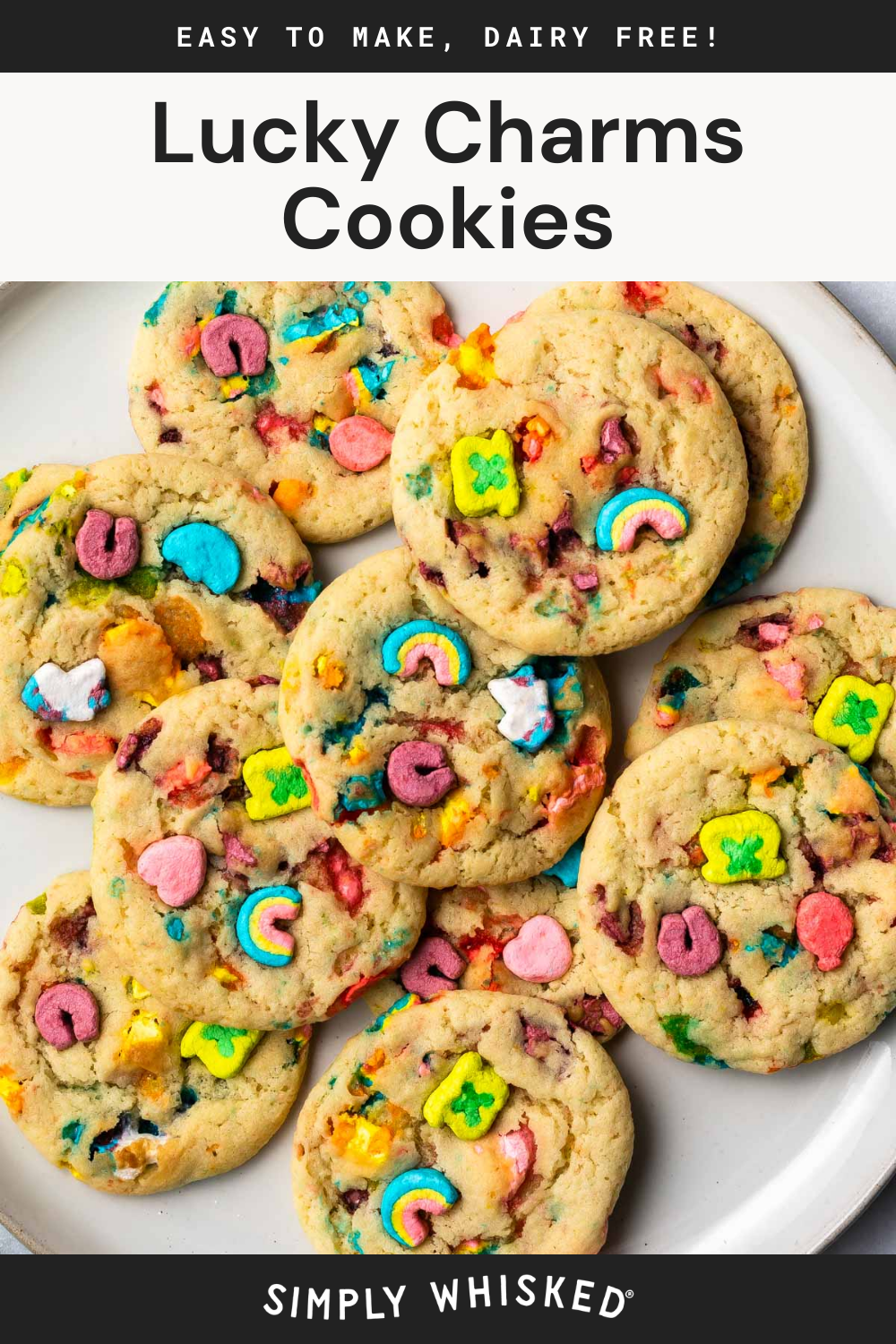 A plate of Lucky Charms cookies topped with colorful marshmallows sits on a white surface. Text above reads Lucky Charms Cookies and Easy to make, dairy free! with Simply Whisked at the bottom.