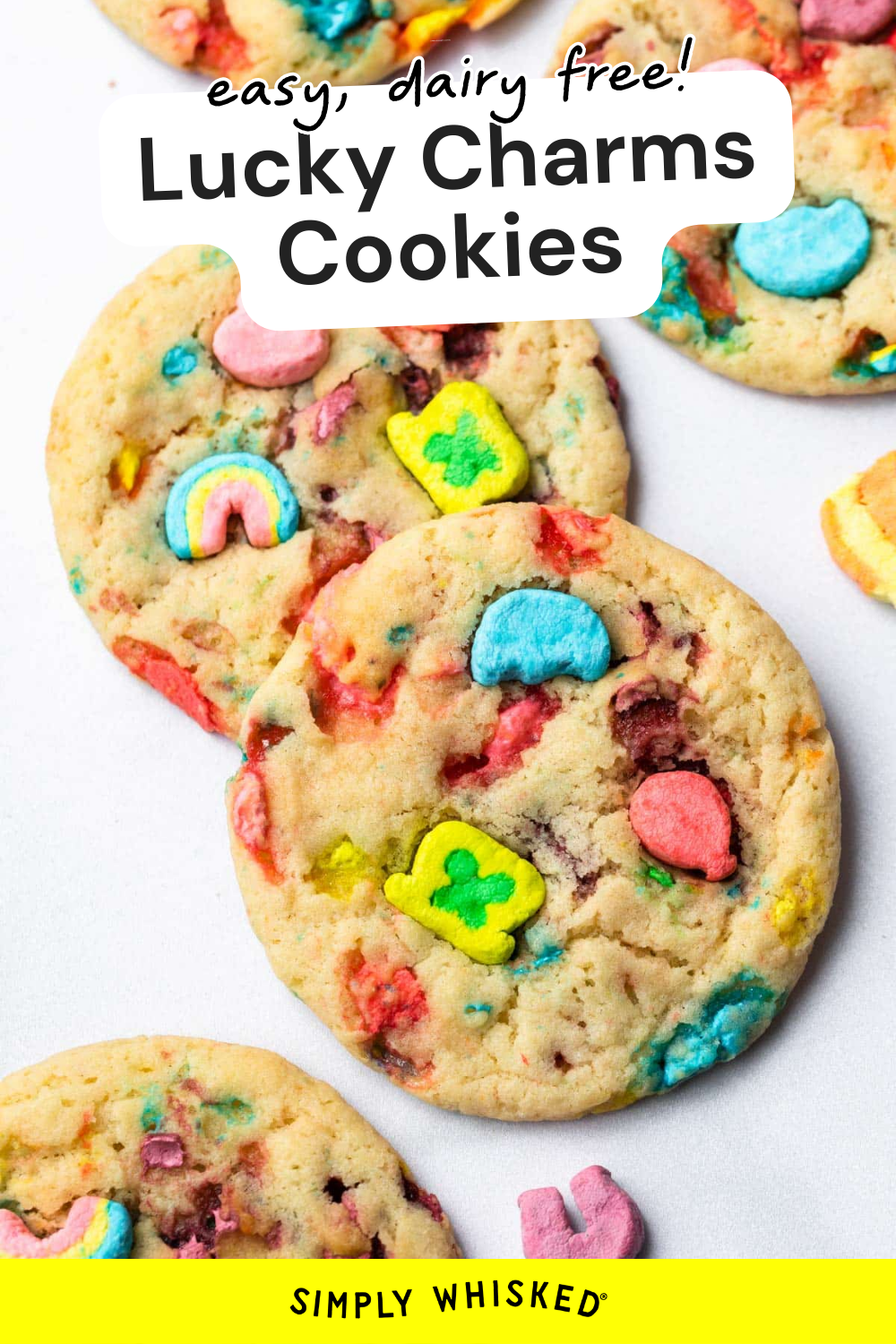 Close-up of colorful Lucky Charms cookies with marshmallows on a white surface. Text above reads easy, dairy free! Lucky Charms Cookies and SIMPLY WHISKED at the bottom.