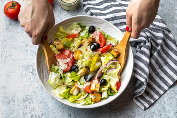 tossing together the salad in a white bowl with wooden utensils